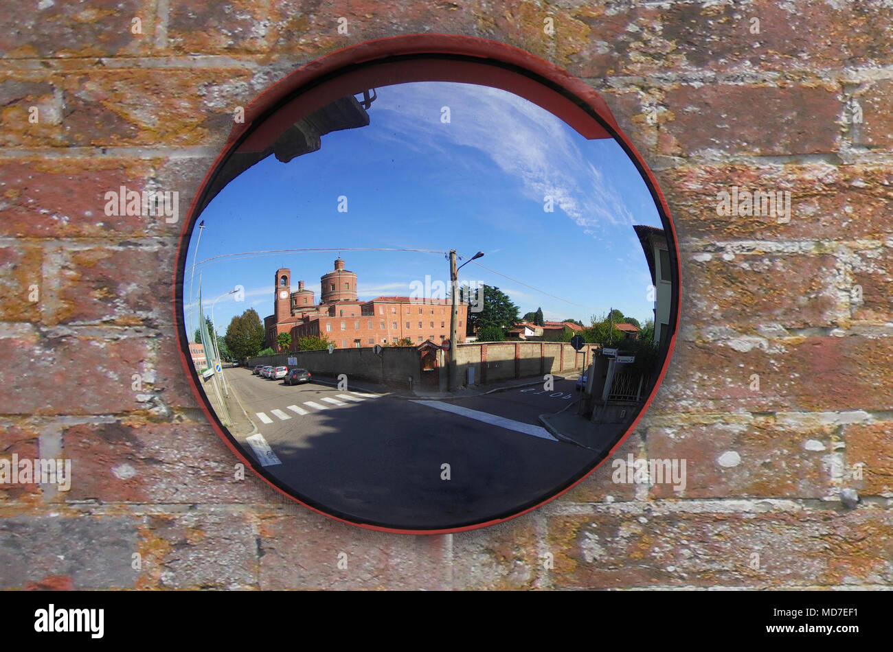 church reflected in a mirror placed at an intersection on an old brick wall in a town near Milan, Italy Stock Photo
