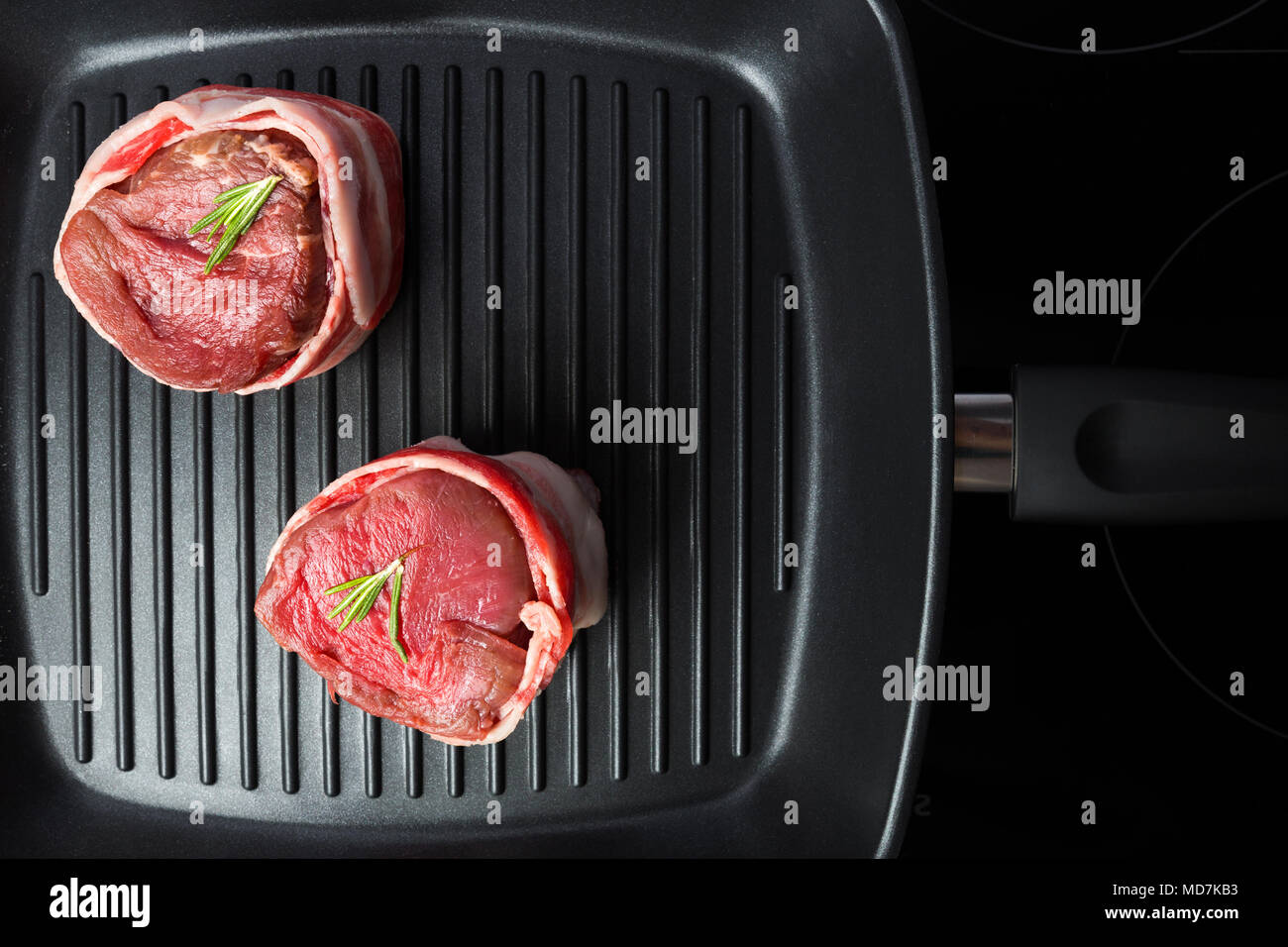 Raw beef steak with bacon and rosemary in grill pan top view. Tasty food background. Stock Photo