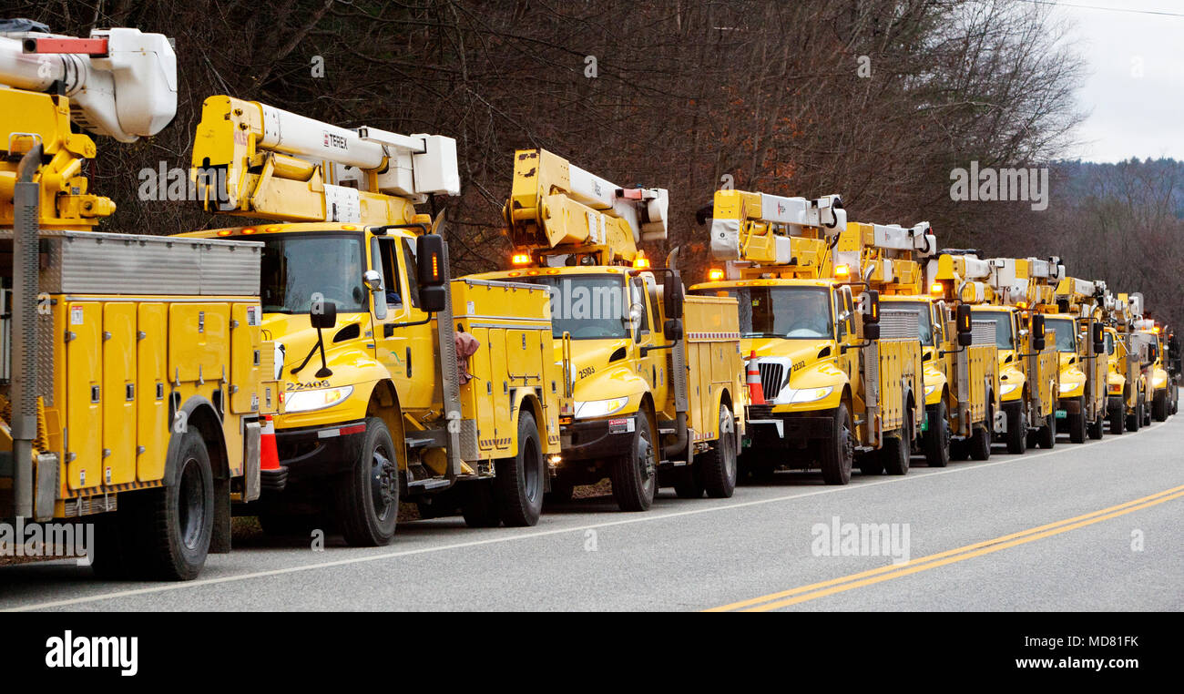A convoy of yellow electric utility trucks in formation heading south