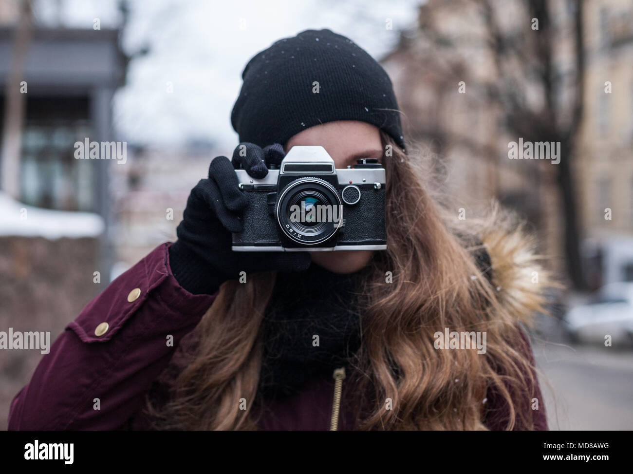 Hipster girl photographer with retro camera taking photo on city street Stock Photo