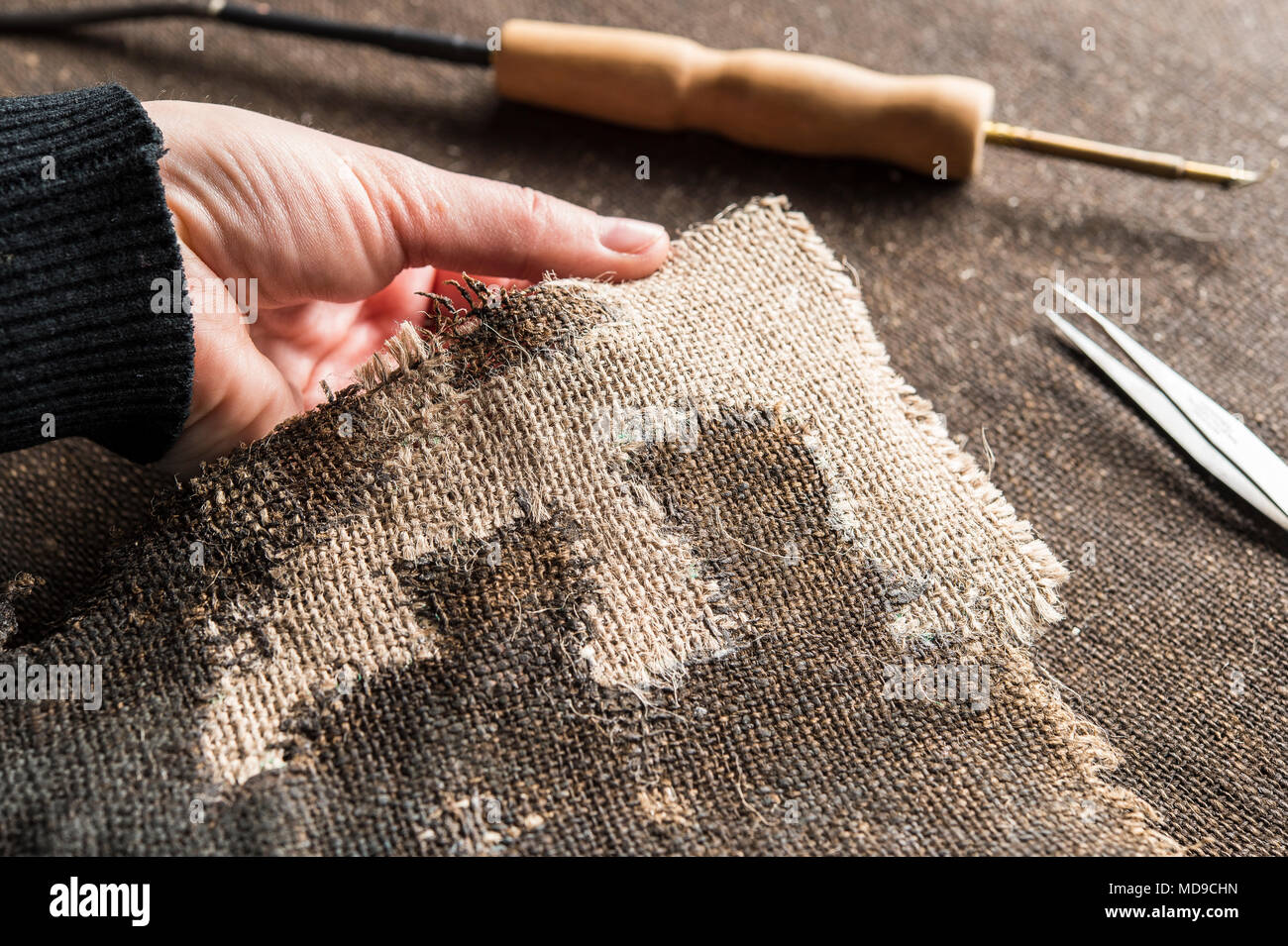 https://c8.alamy.com/comp/MD9CHN/restoration-studio-restorer-hand-holds-the-finished-processed-and-woven-linen-piece-behind-heating-spatula-and-tweezers-MD9CHN.jpg