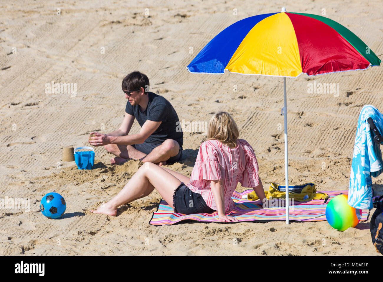 Bournemouth, Dorset, UK. 19th April 2018. UK weather: lovely warm sunny day at Bournemouth beaches with clear blue skies and unbroken sunshine, as visitors head to the seaside to enjoy the warmest day of the year so far. Couple relaxing on the beach under colourful parasol. Credit: Carolyn Jenkins/Alamy Live News Stock Photo