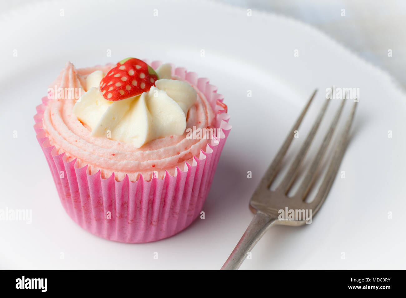 Pink strawberry cupcake on white plate with fork Stock Photo