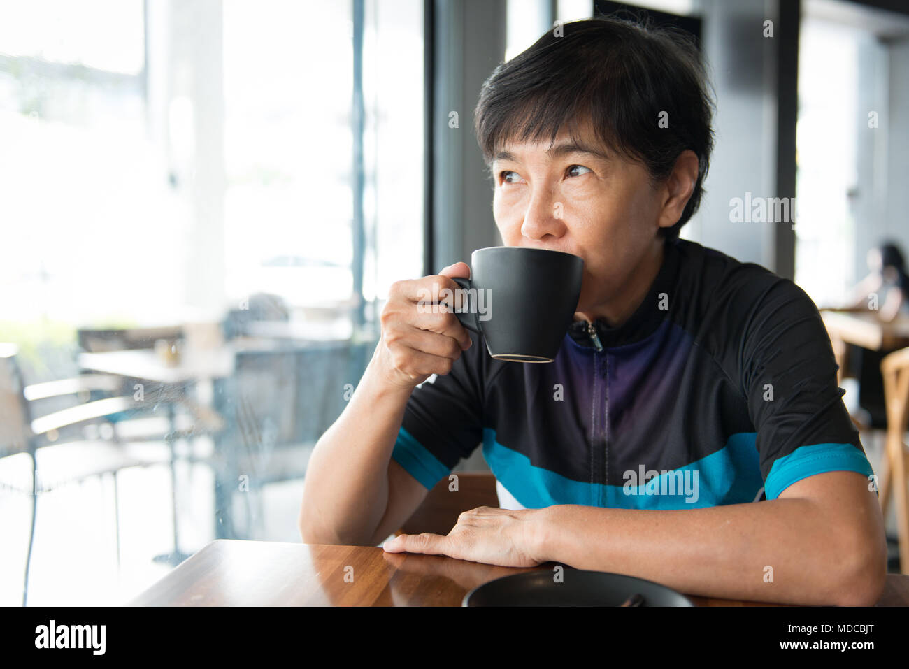 Senior Asian woman with coffee in cycling jersey Stock Photo