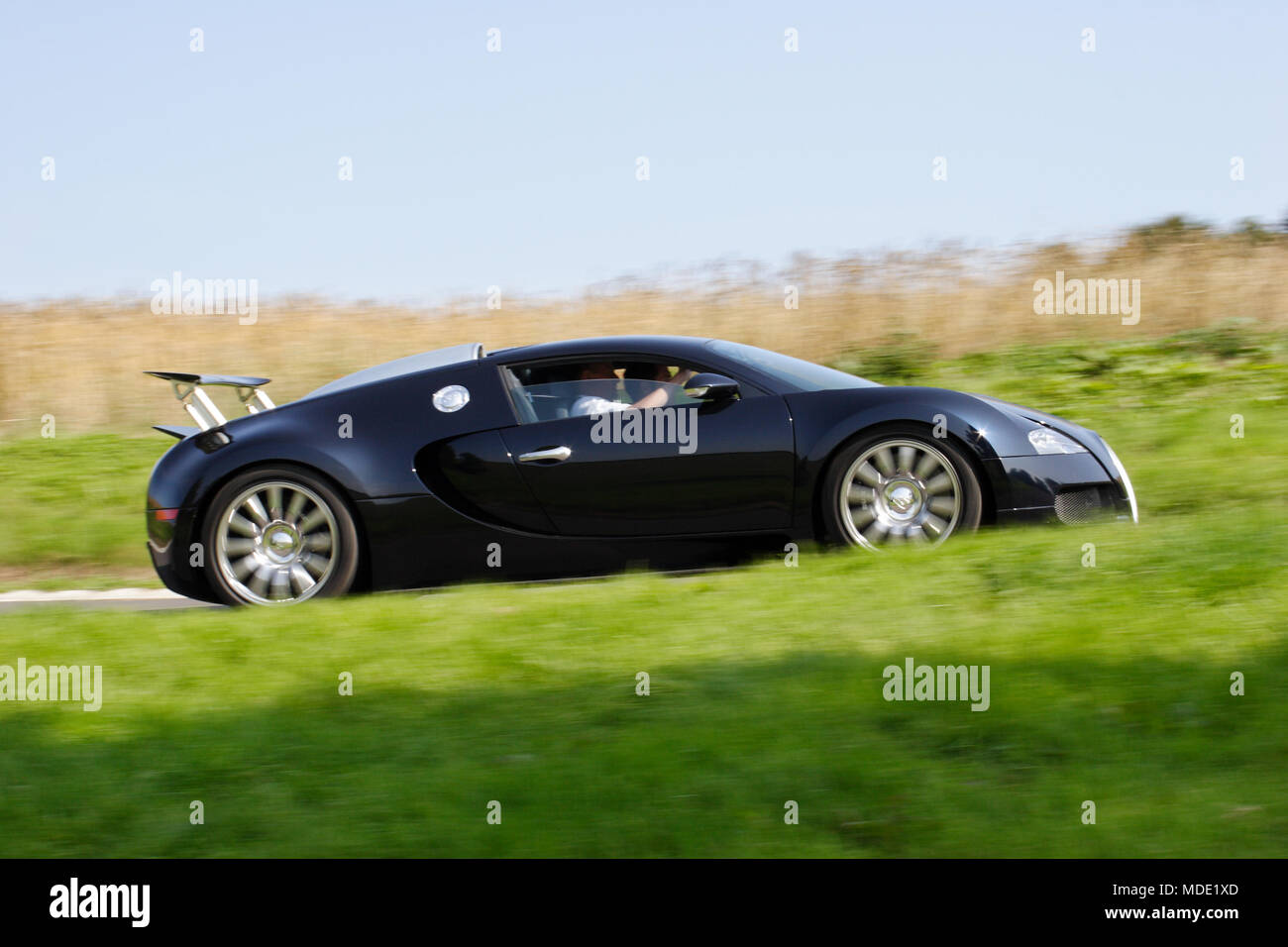 Low angle profile (side view) of Black Bugatti Veyron million £ pound hyper car hypercar driving fast on a country road. Stock Photo