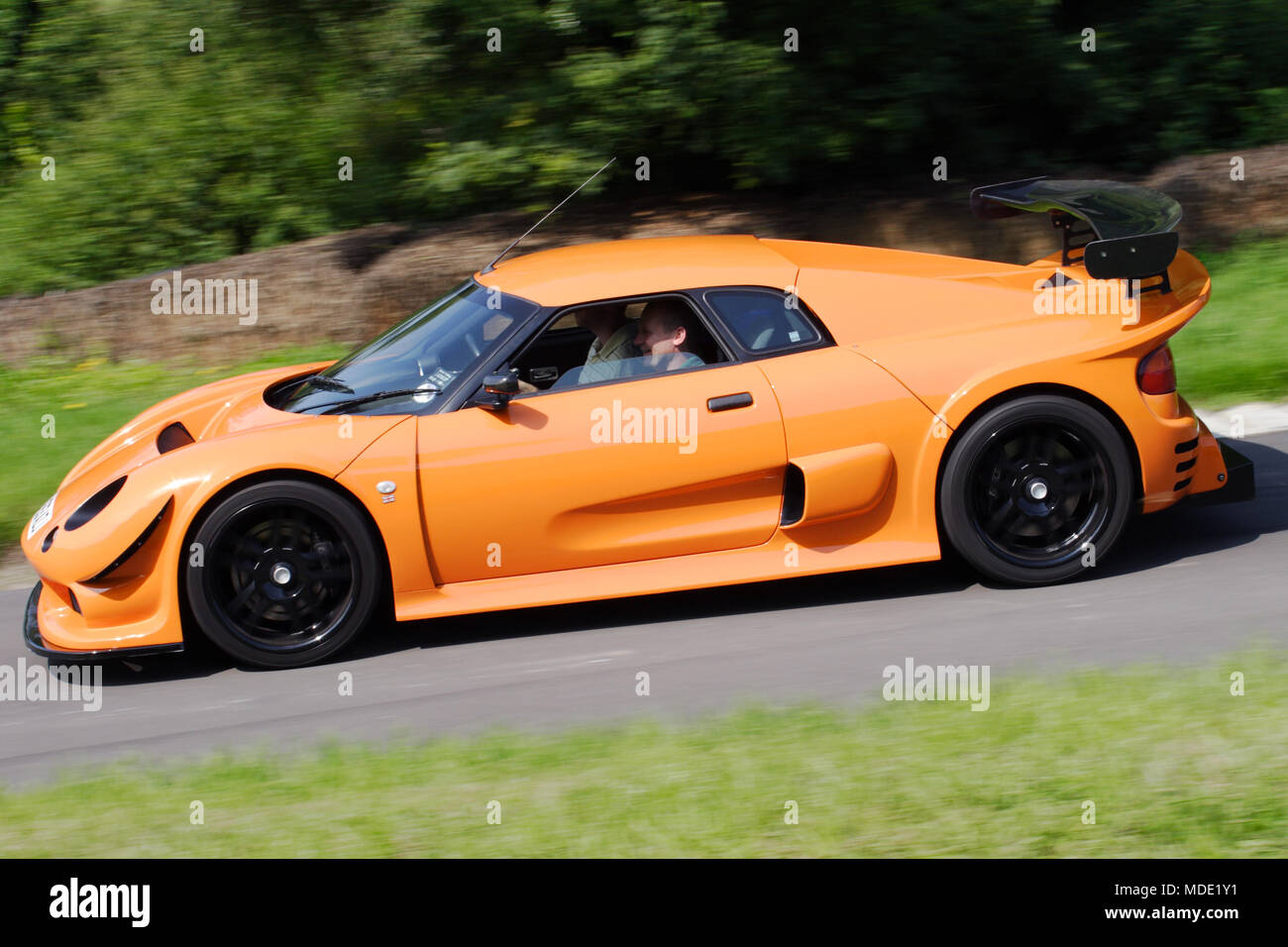Profile (side view) of a fluorescent bright orange Noble M12 GT0-3R British supercar sports car driving fast or racing Stock Photo