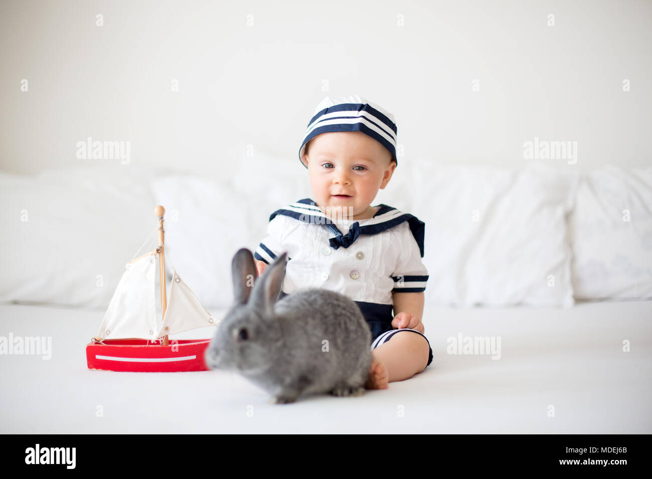 Cute baby boy dressed in marine clothes playing with wooden boat