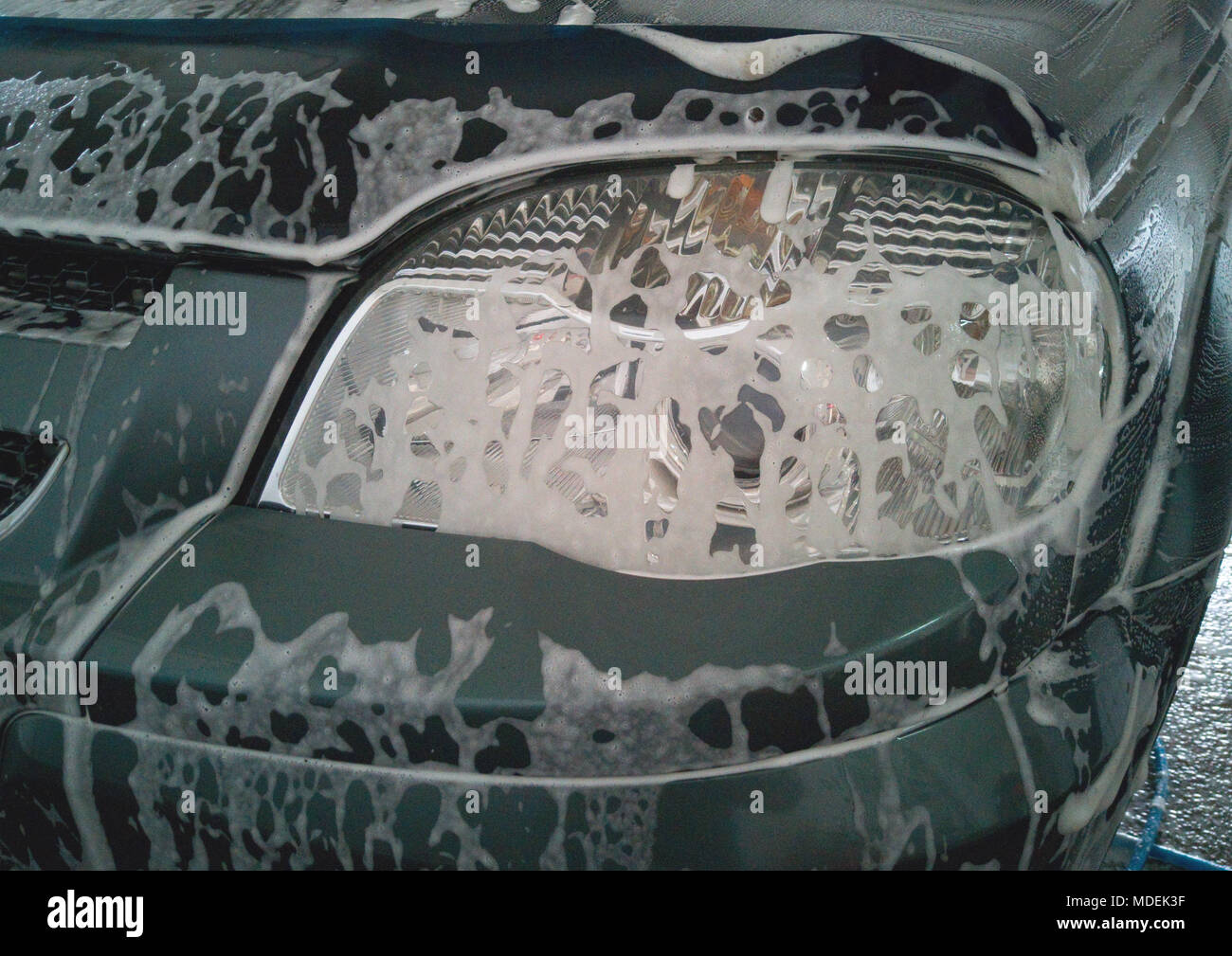 Car wash. Soap foam dissolved dirt on the left front headlight of the car Stock Photo