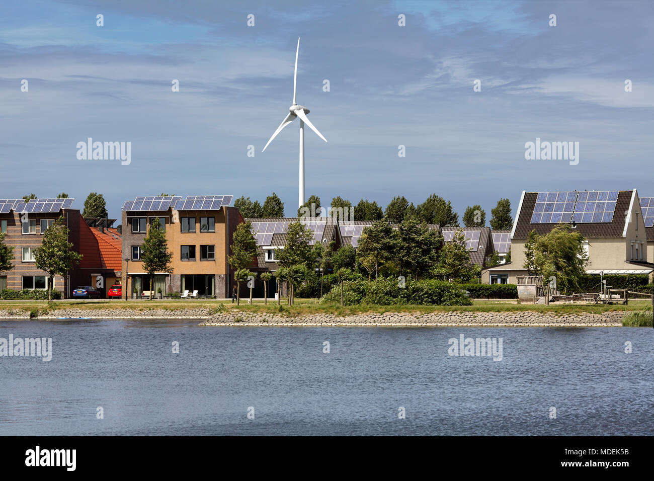 Houses topped with photovoltaic cells with a wind turbine behind in Stad van de Zon (City of the Sun), a sustainable suburb of Heerhugowaard, Holland. Stock Photo