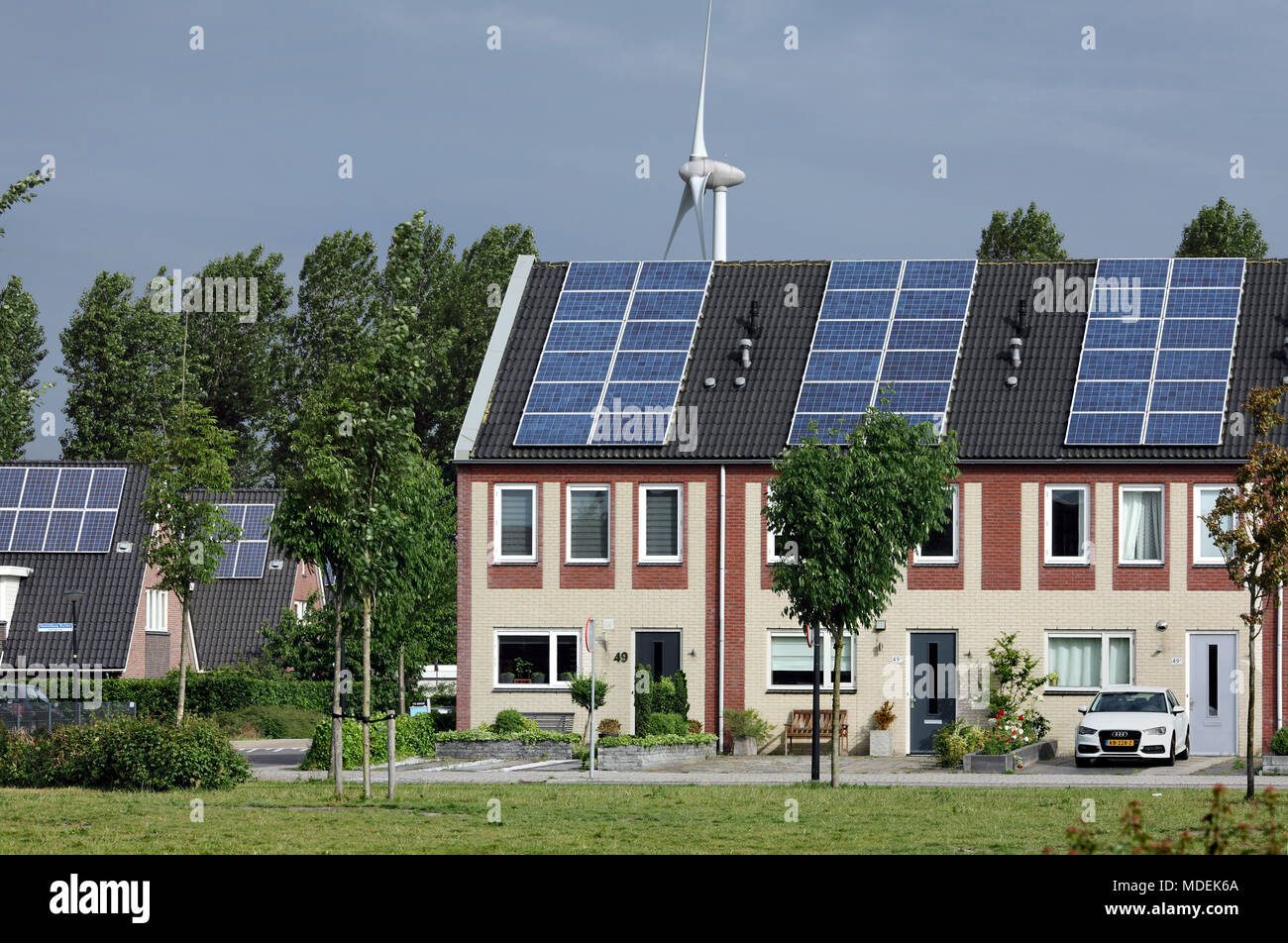 Houses topped with photovoltaic cells with a wind turbine behind in Stad van de Zon (City of the Sun), a sustainable suburb of Heerhugowaard, Holland. Stock Photo