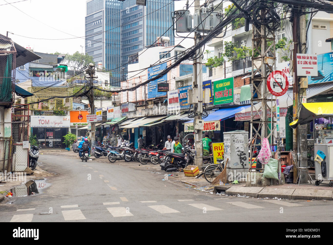 A tangle of overhead power lines and a short street with parked motorbikes and shops in Ho Chi Minh City, Vietnam. Stock Photo