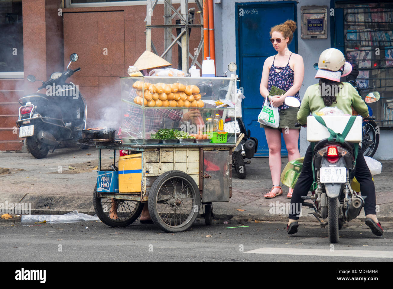 A tourist buying banh mi from a street vendor in Ho Chi MInh City, Vietnam. Stock Photo