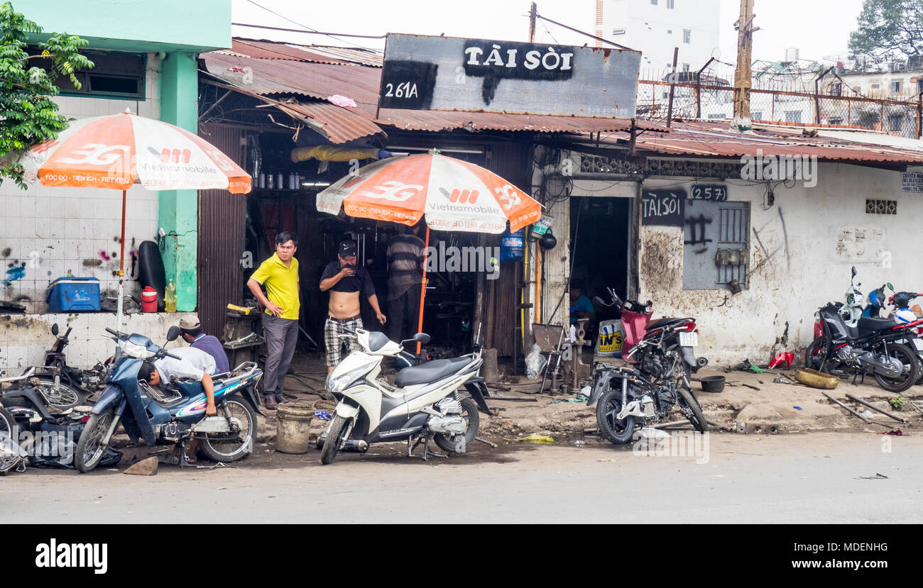 Vietnamese motorcycle mechanics working on the pavement and client standing outside the workshop in Ho Chi Minh City, Vietnam. Stock Photo