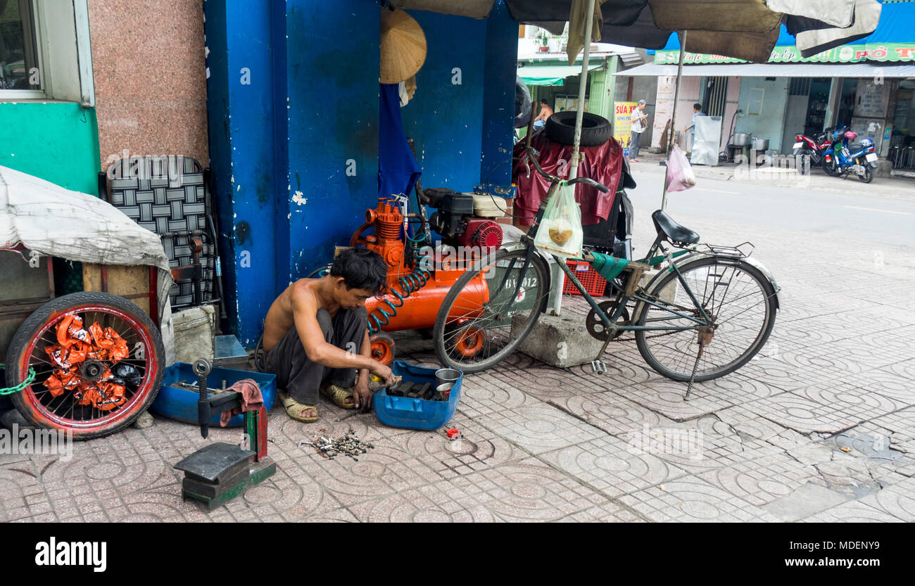 A Vietnamese bicycle repairman repairing a bike on the side walk in Ho Chi Minh City, Vietnam. Stock Photo