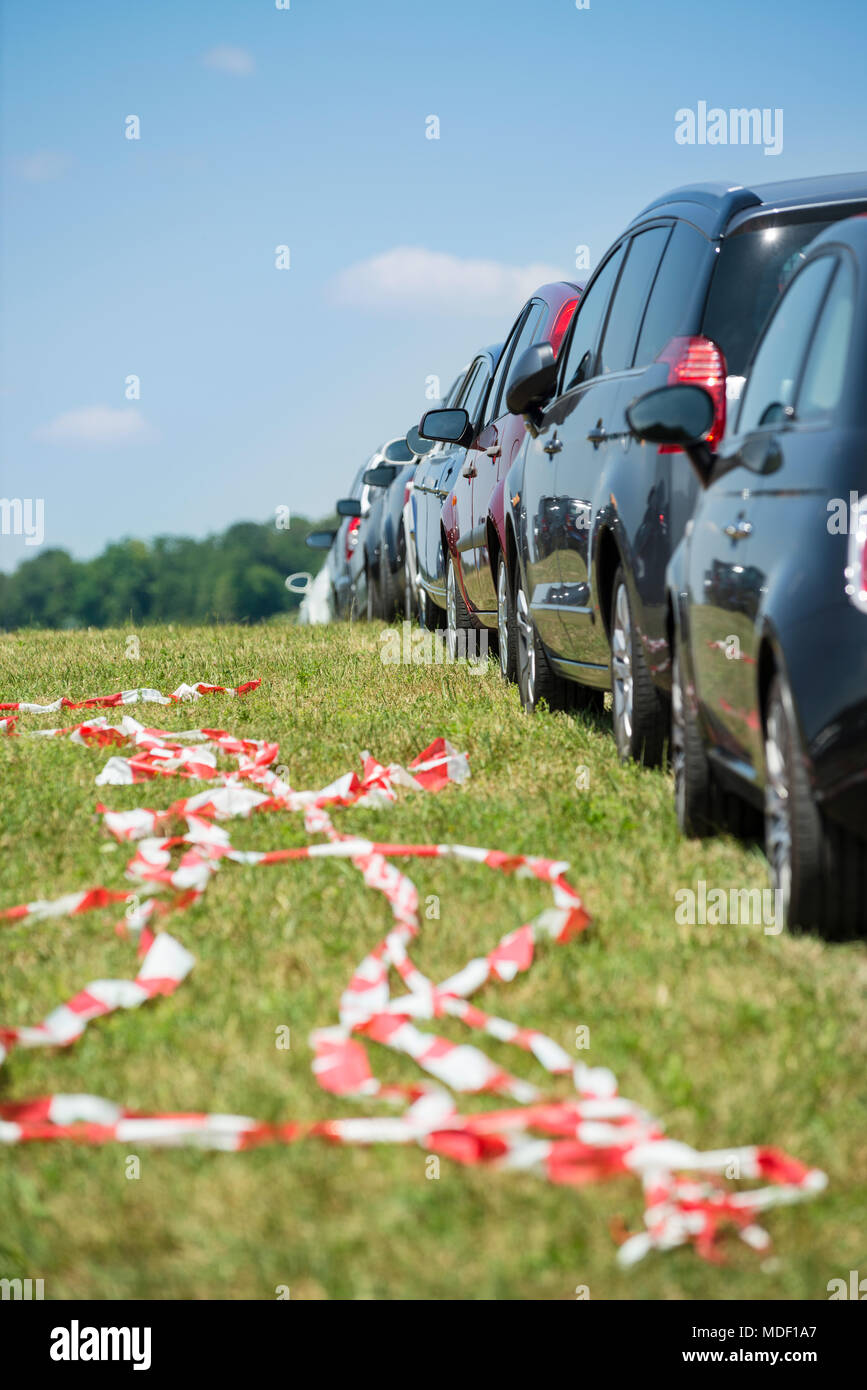 Cars parking in line in the green with red and white barrier tape at what might be a festival Stock Photo