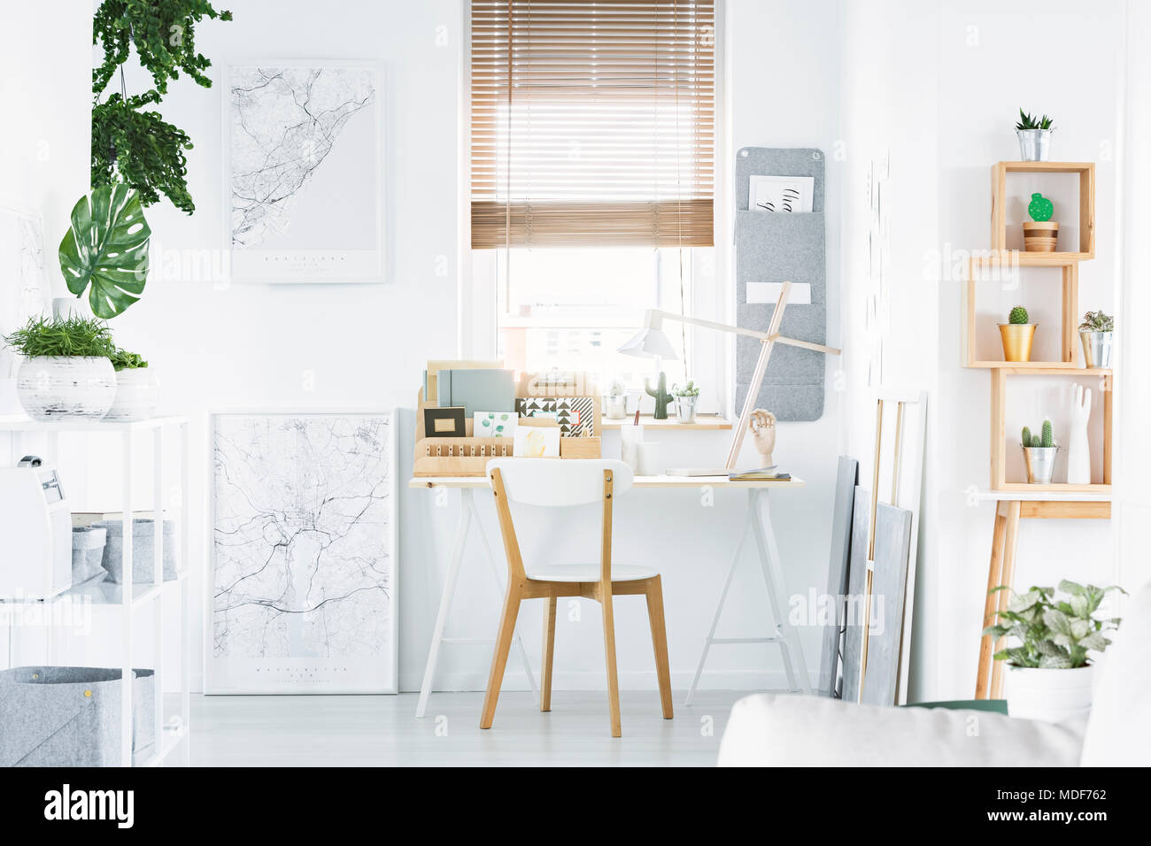 Bright home office interior with desk, wooden chair, shelf, plants and posters Stock Photo