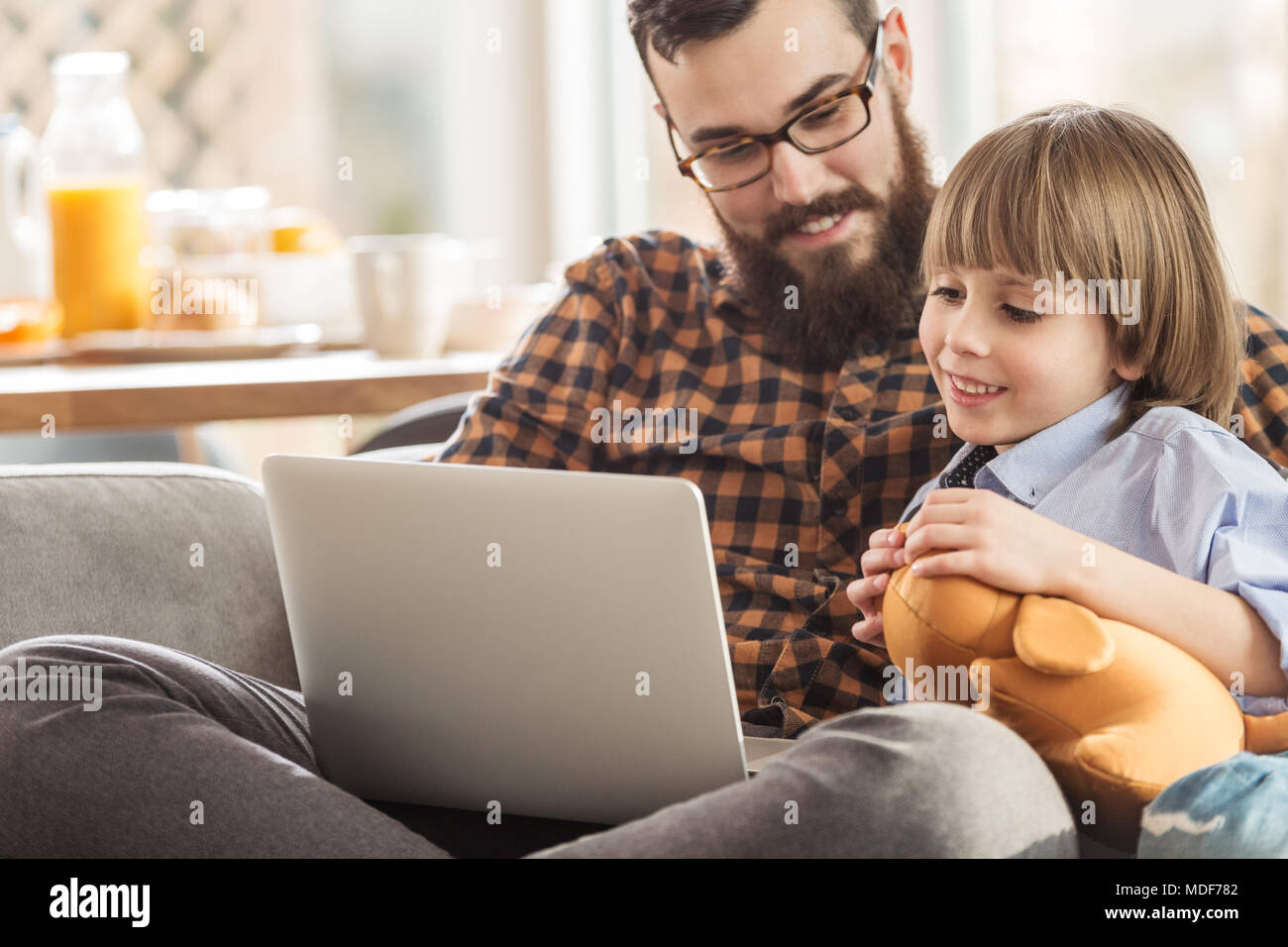 Smiling father and son watching a movie together while sitting on a sofa Stock Photo
