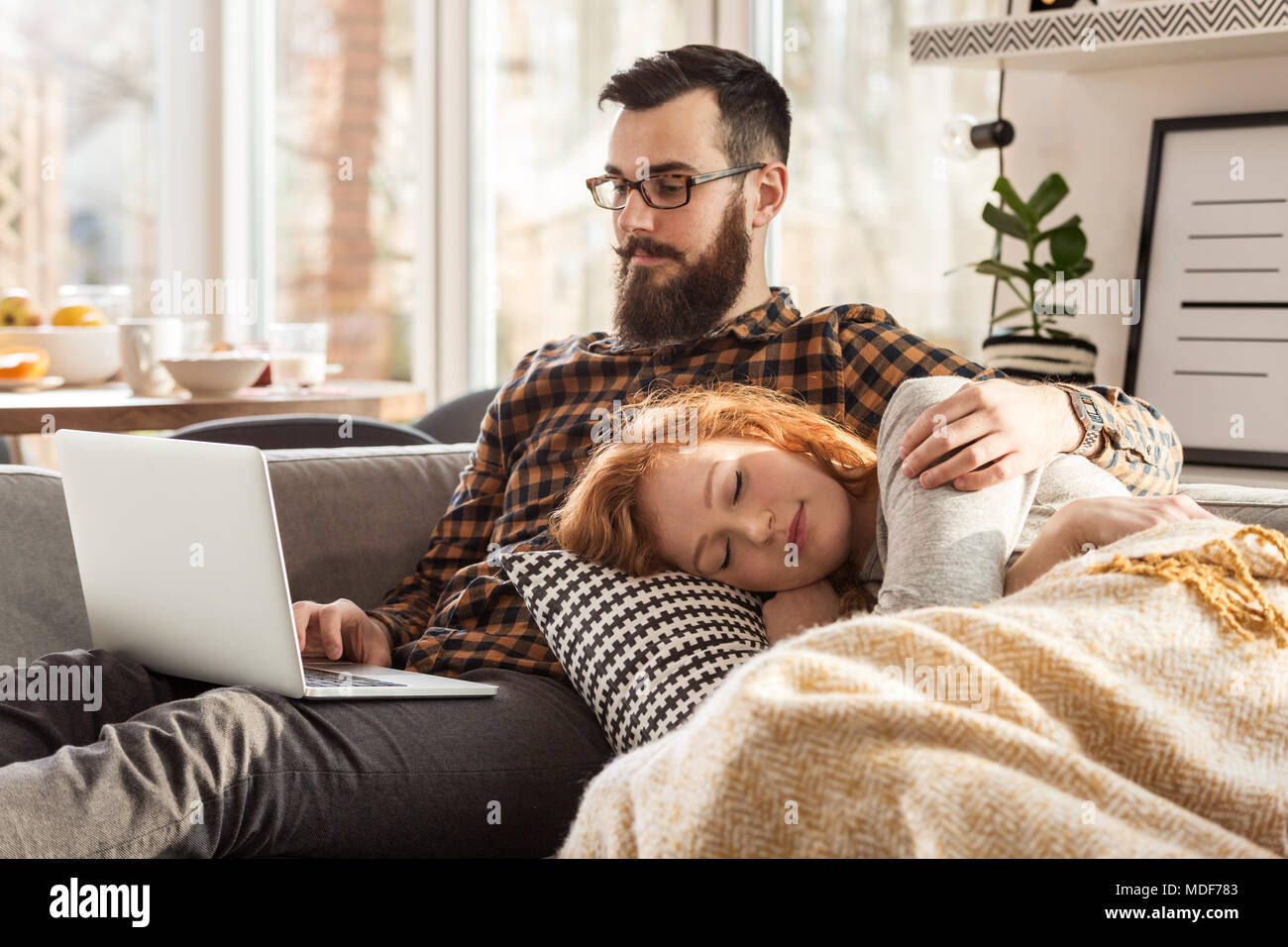 Young girlfriend sleeping on her boyfriend's lap while he is using his computer Stock Photo