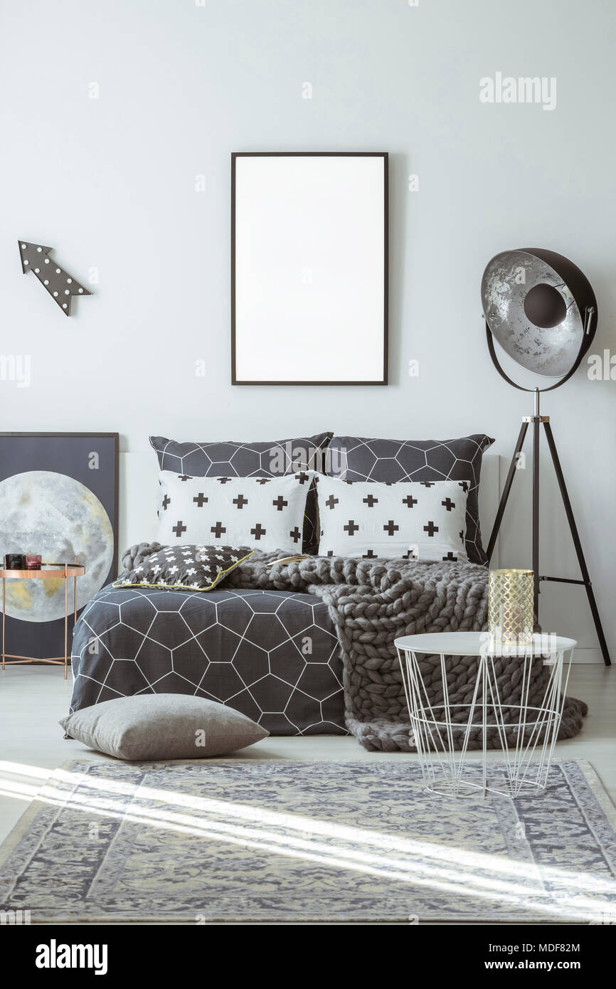 Lamp next to patterned bed in bedroom interior with mockup of white