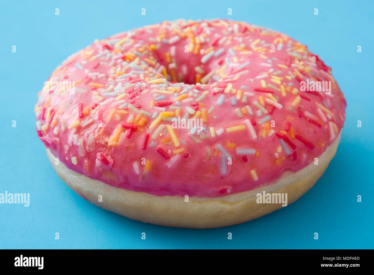 Pink frosted donut with colorful sprinkles on blue background Stock ...