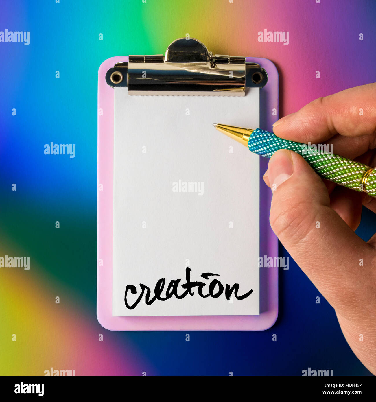 Writing pad with hand and pen poised to draw, write, sketch and be creative, isolated and presented on a colourful background, for creative design Stock Photo