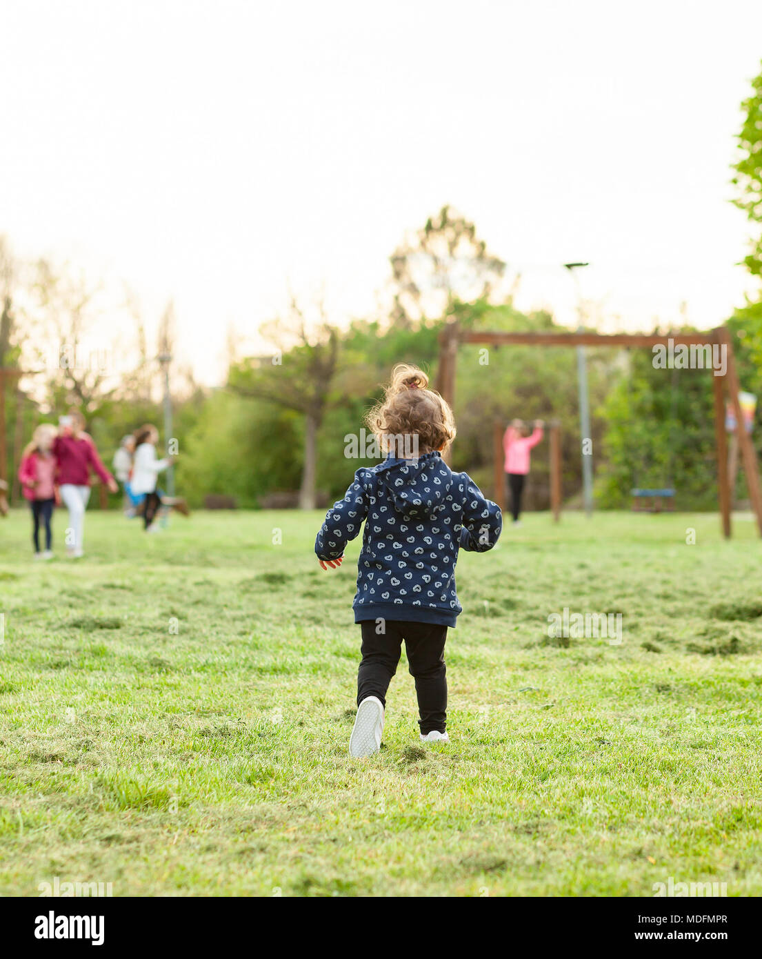 Little girl runs from behind in the park playing with other children