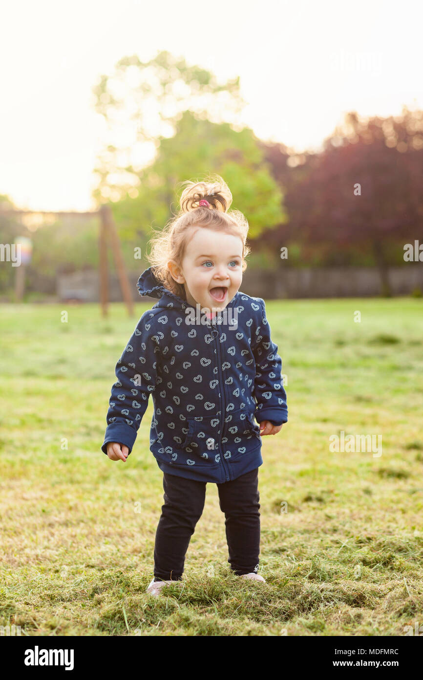 Little baby girl plays happy in the park outdoors in the spring against the backlight. Stock Photo