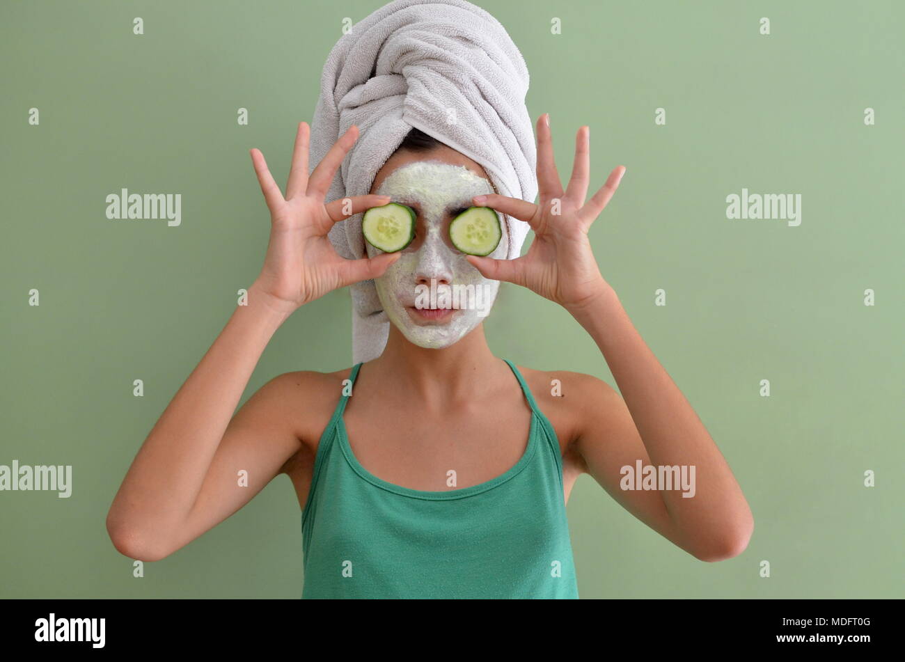 Teenage girl with a face mask on holding cucumber slices in front of her eyes Stock Photo