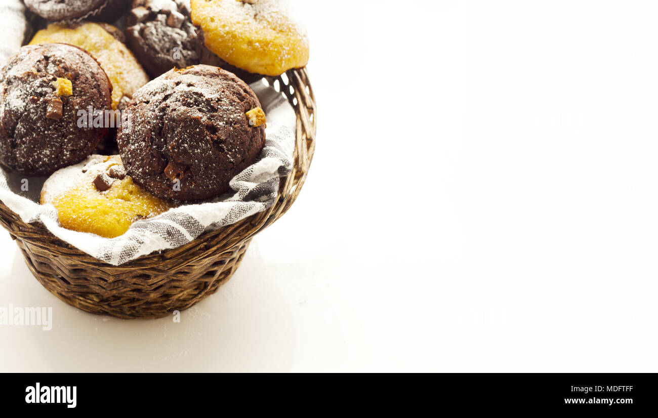 A selection of muffins in wicker basket on white work surface, shot at angle and tight crop for ad space Stock Photo