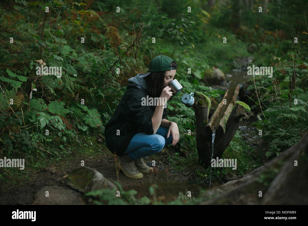 Woman crouching by a stream drinking water Stock Photo