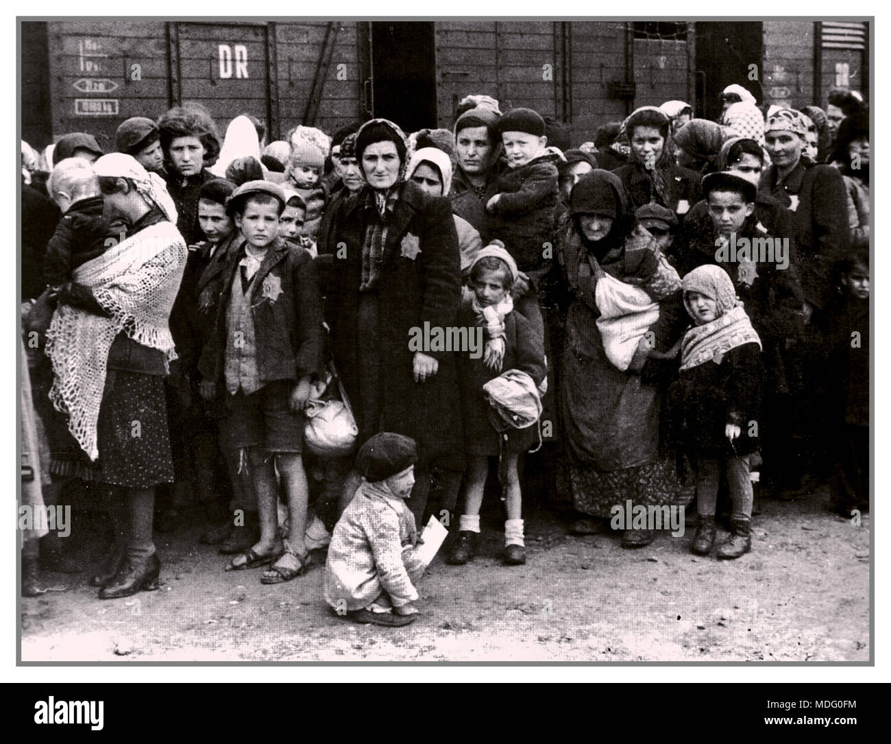 German Nazi Holocaust death camp Auschwitz in Poland, arrival of Hungarian Jews of all ages, wearing the instructed Jewish Star of David. Waiting on the Nazi ‘grading’ system of a life with torture and starvation or summary death in gas chambers. Summer 1944.World War II Stock Photo
