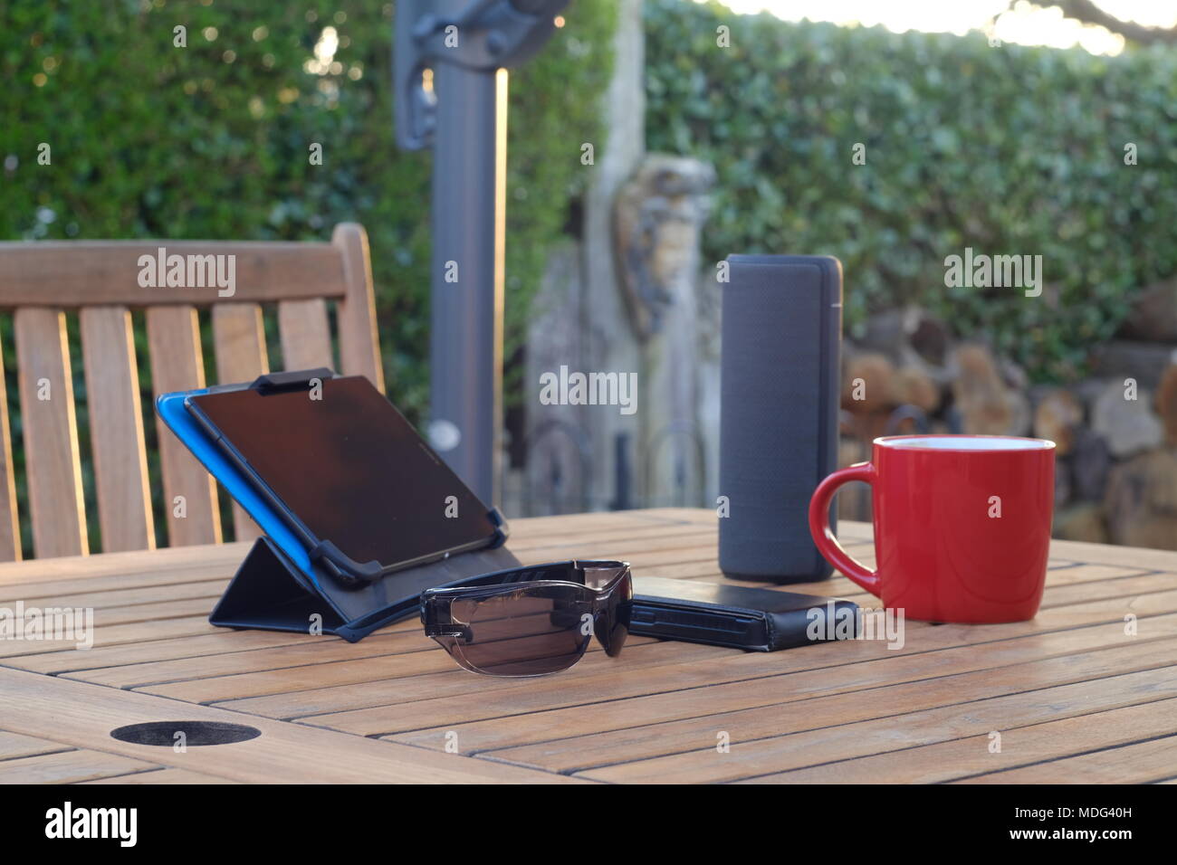 A selection of technology items on a wooden garden table with a parasol ...