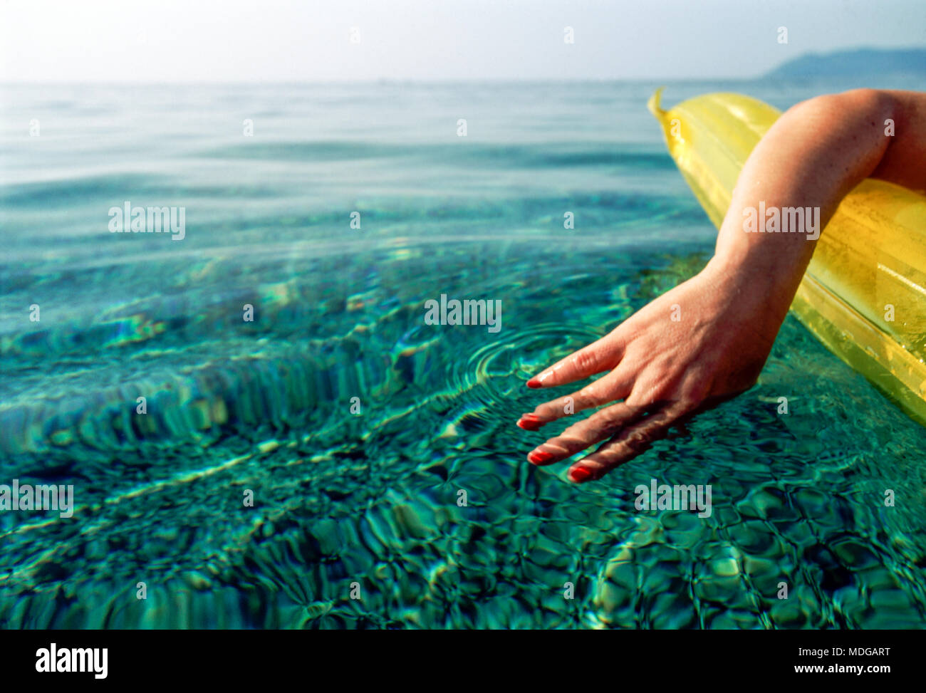 Sardinia, Italy; woman on a lilo with hand trailing in the water Stock Photo