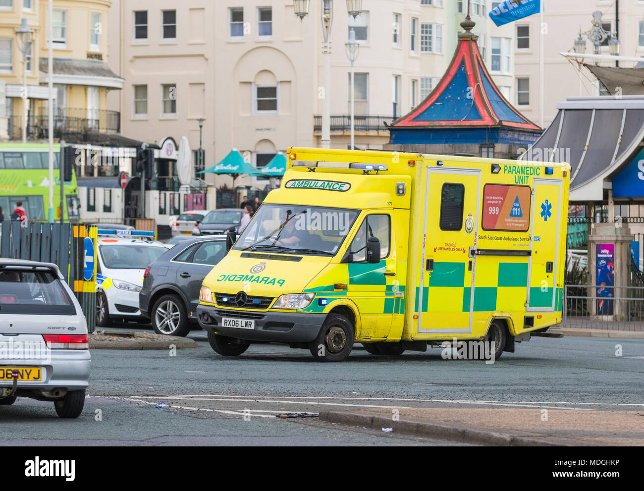 British NHS Ambulance in busy traffic on a roundabout, on call with lights flashing in Brighton, East Sussex, UK. Mercedes Sprinter 416 CDI from 2006. Stock Photo