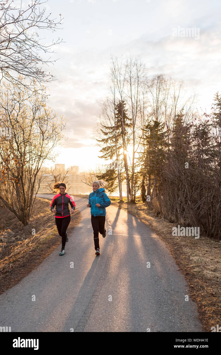 Two young women running on a trail at sunrise; Anchorage, Alaska, United States of America Stock Photo