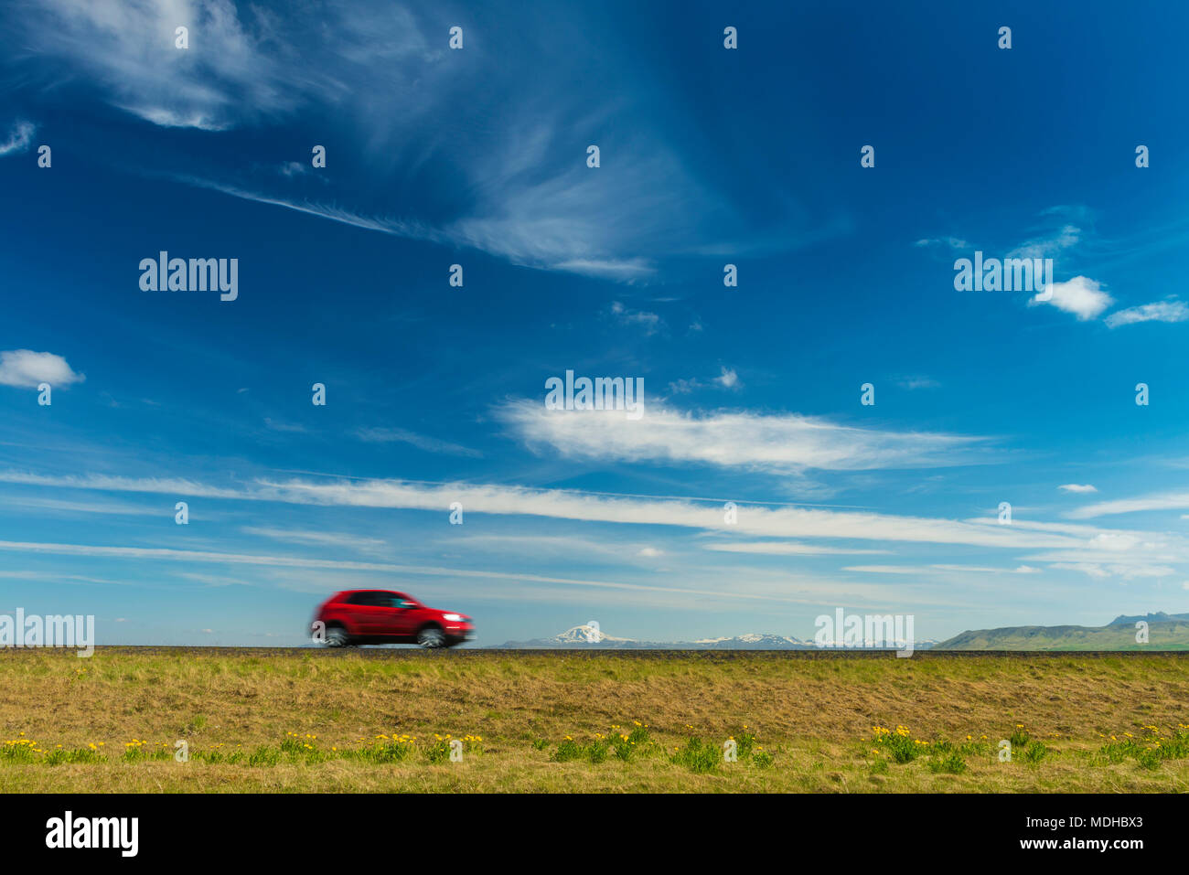 Red car driving on open road near Hella with Hekla volcano in the distance; Iceland Stock Photo