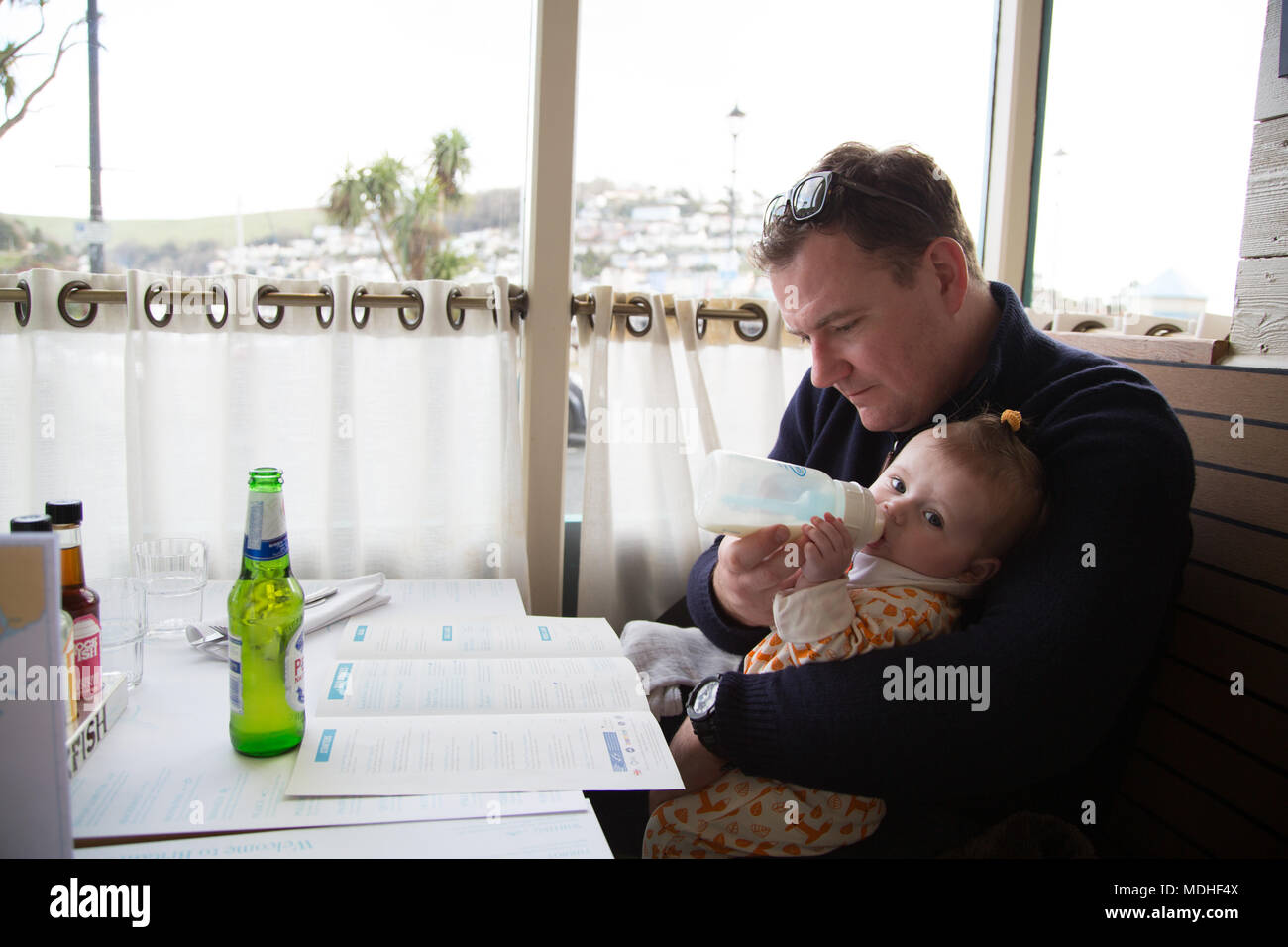 Dad feeding baby bottle in restaurant Stock Photo