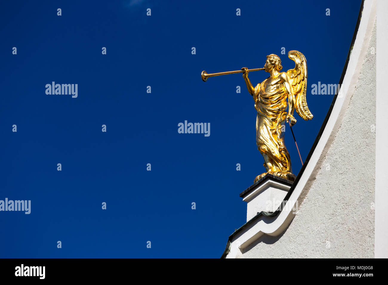 Gold winged angel sculpture with trumpet on top of white church against a blue sky; San Candido, Bolzano, Italy Stock Photo