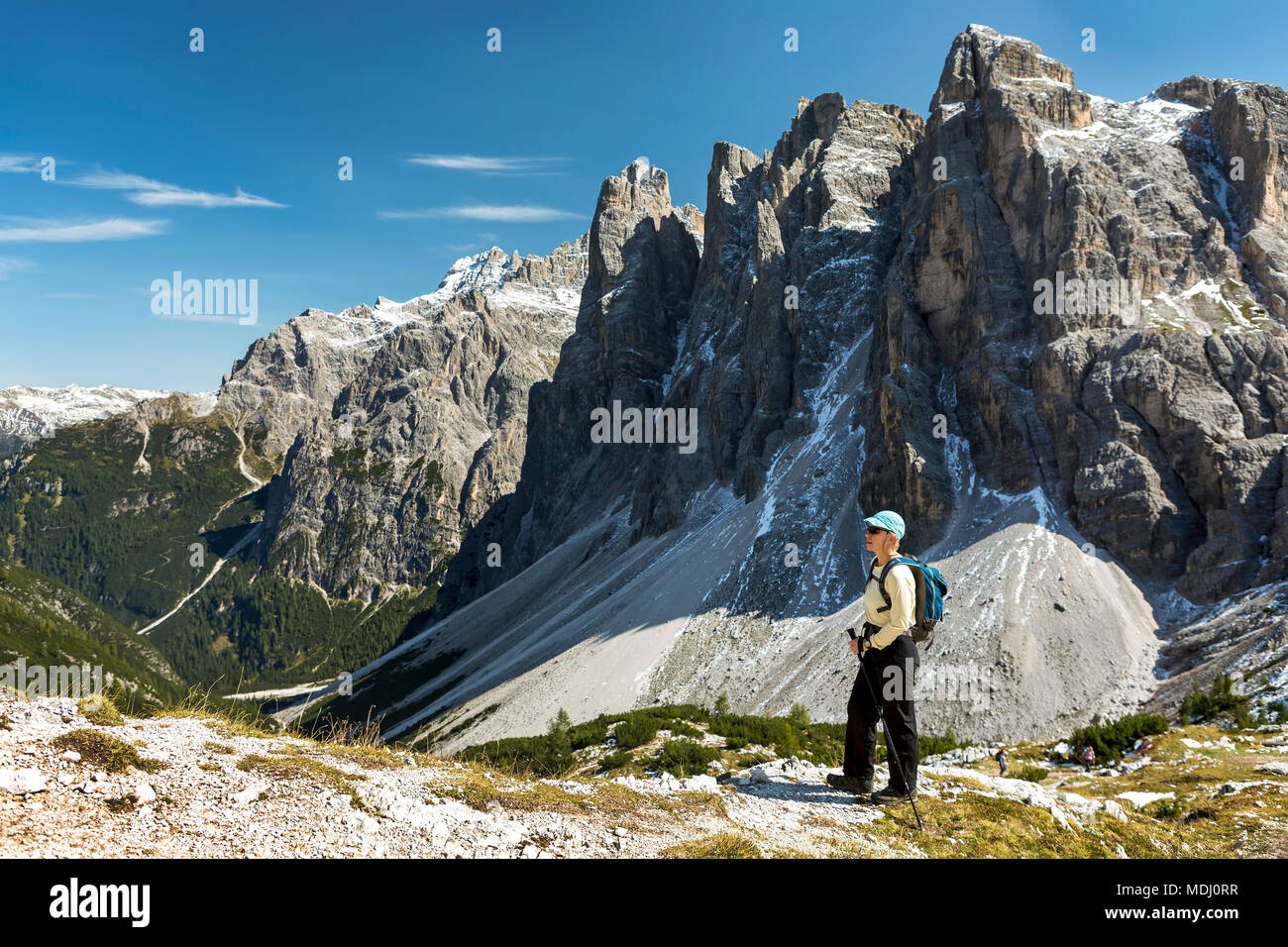 Female hiker overlooking valley against rugged mountain range and blue sky; Sesto, Bolzano, Italy Stock Photo
