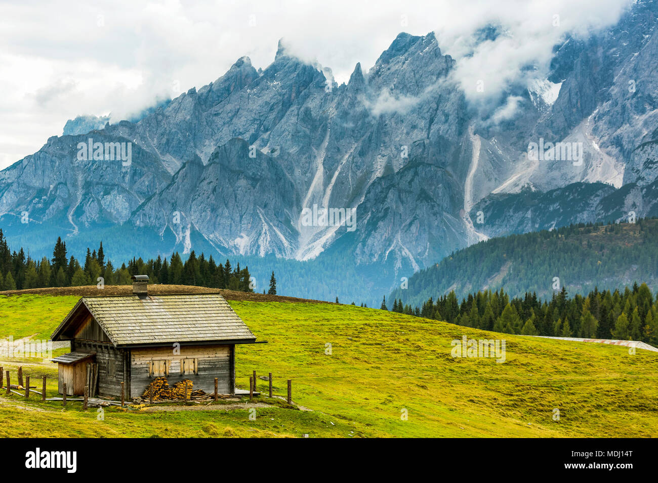Wooden barn on top of alpine meadow with rugged mountain range in the background; Sesto, Bolzano, Italy Stock Photo