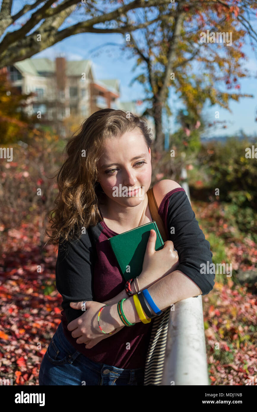 A young woman sits on a park bench clutching a book to her chest; New Westminster, British Columbia, Canada Stock Photo