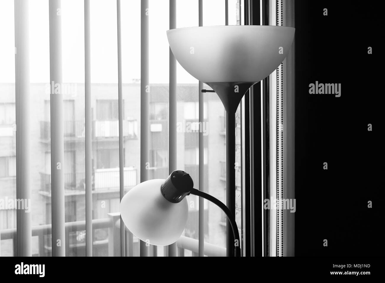 Fancy floor lamps standing near a window in black & white key. A large window with modern blinds and stylish lamps. Stylish living room interior. Stock Photo