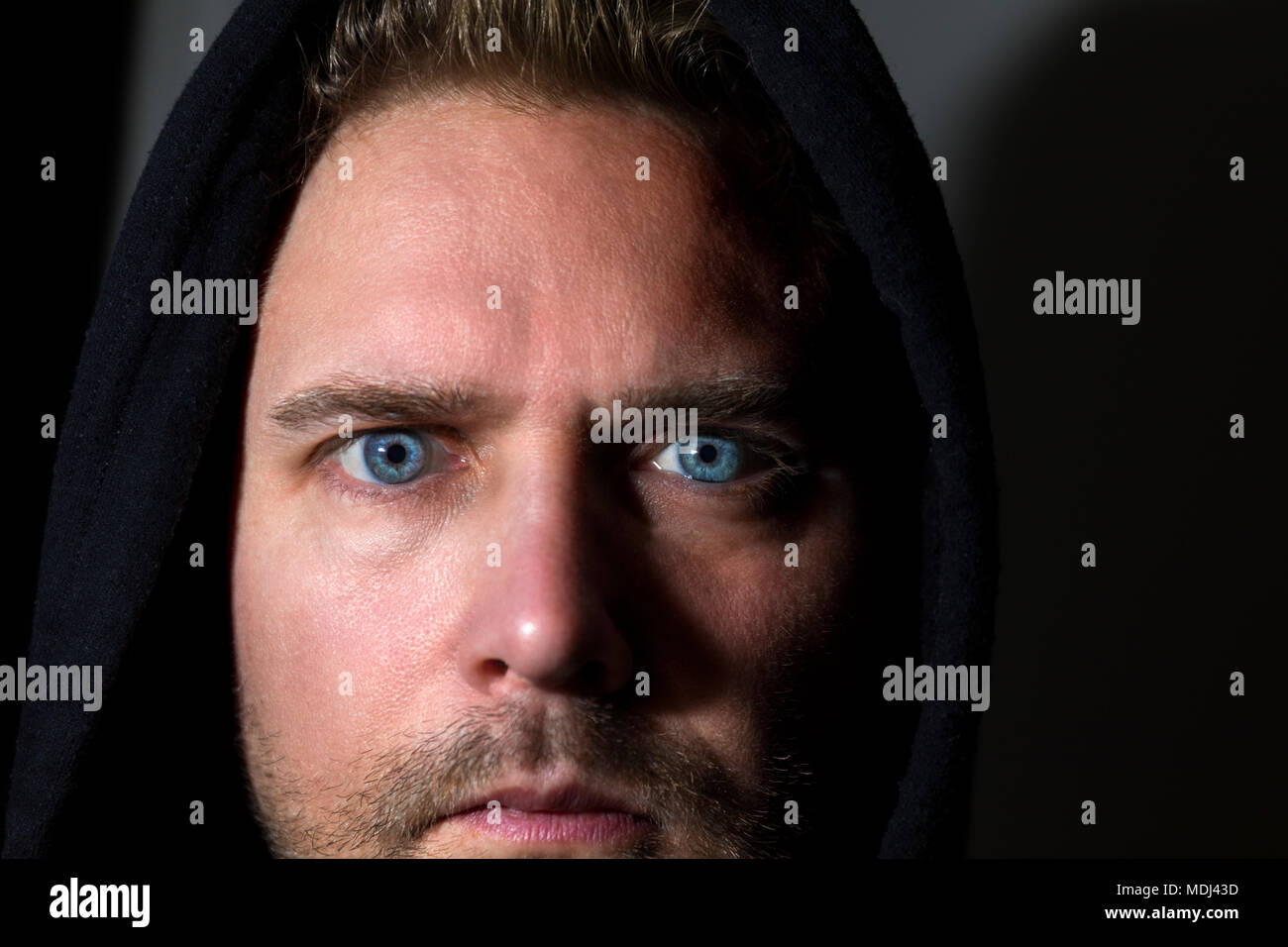 Close up face portrait of mid adult caucasian man with striking piercing blue eyes against a dark background  Model Release: Yes. Property Release: No. Stock Photo
