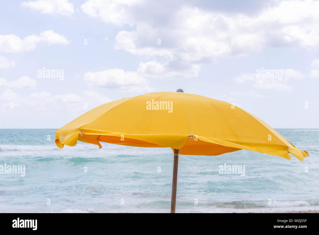 Yellow umbrella at the beach, beautiful sea and sky image. Windy summer day with waves. Miami