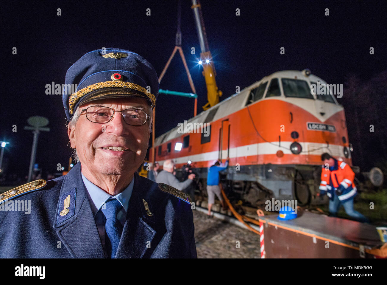 19 April 2018, Germany, Gadebusch: Locomotive driver Peter Falow smiles in his old Reichsbahn uniform as two cranes lift a 78 tonne diesel locomotive of the model V-180 into the railway museum outside the local train station. The so-called 'cigar' locomotive was built in 1967. Photo: Jens Büttner/dpa-Zentralbild/dpa Stock Photo