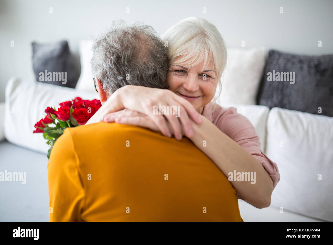 Portrait of senior lady hugging her husband holding bunch of roses Stock Photo