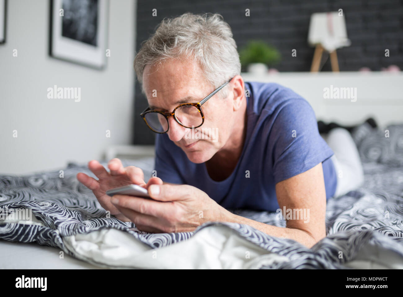 Portrait of senior man lying on bed using smartphone Stock Photo