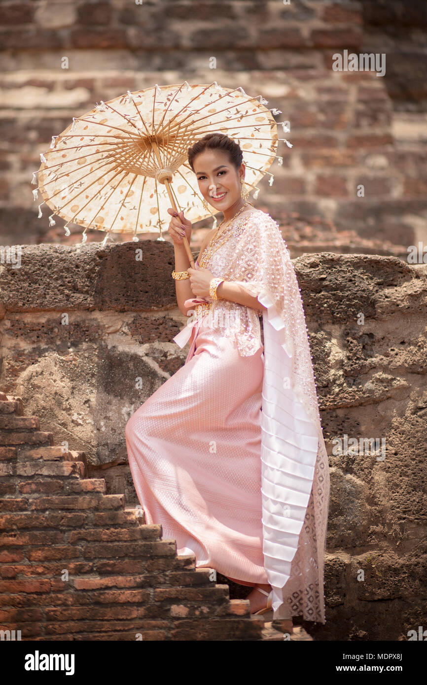 beatiful asian woman wearing thai traditon clothes style with wood umbrella  toothy smiling standing in ayutthaya heritage place Stock Photo