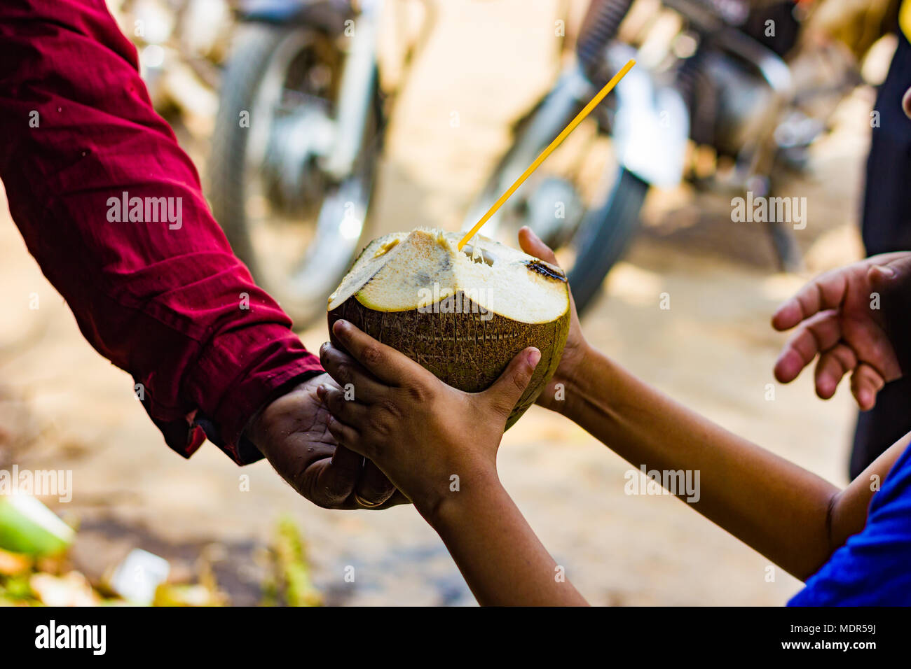 coconut water in coconut with straw handed over to a kid by seller. natural tropical drink. Stock Photo