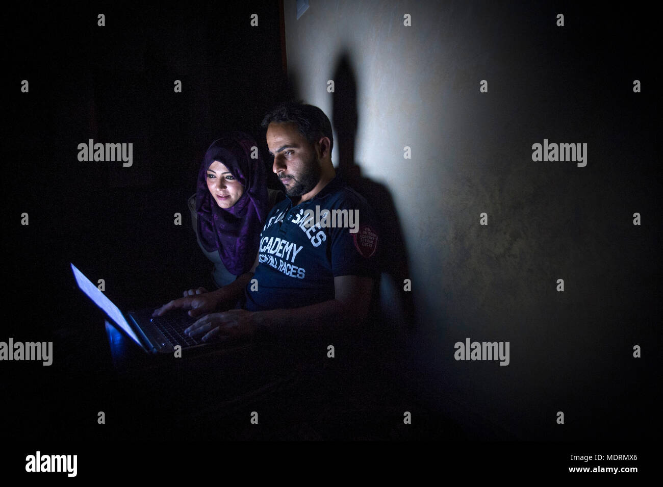IT specialists Mohammad and Tala Al-Nagi try to work at home through a power cut in Gaza with the remaining battery in their lap top computers. Stock Photo